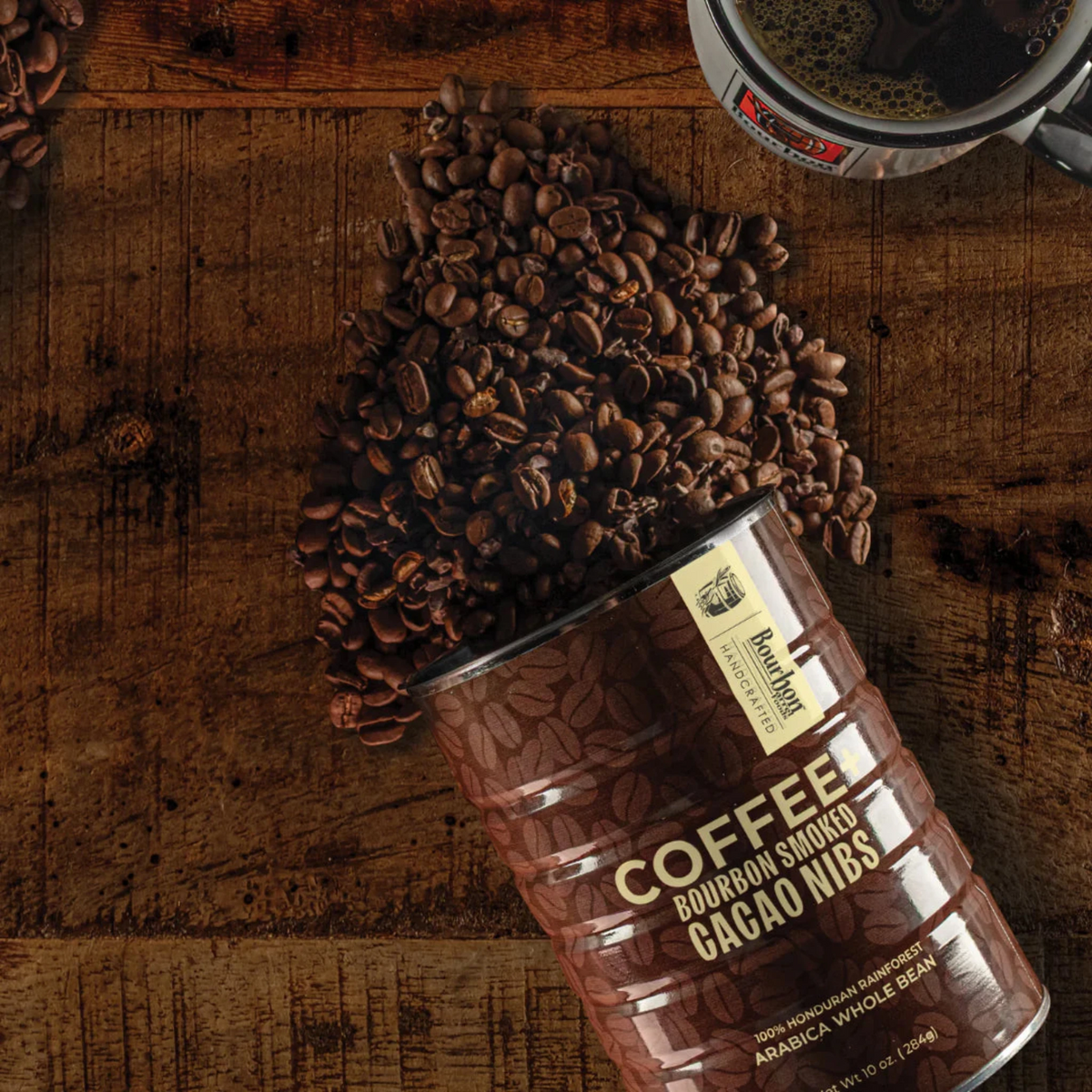 Coffee beans spilling out of a can labeled 'Bourbon Smoked Cacao Nibs' on a wooden surface.