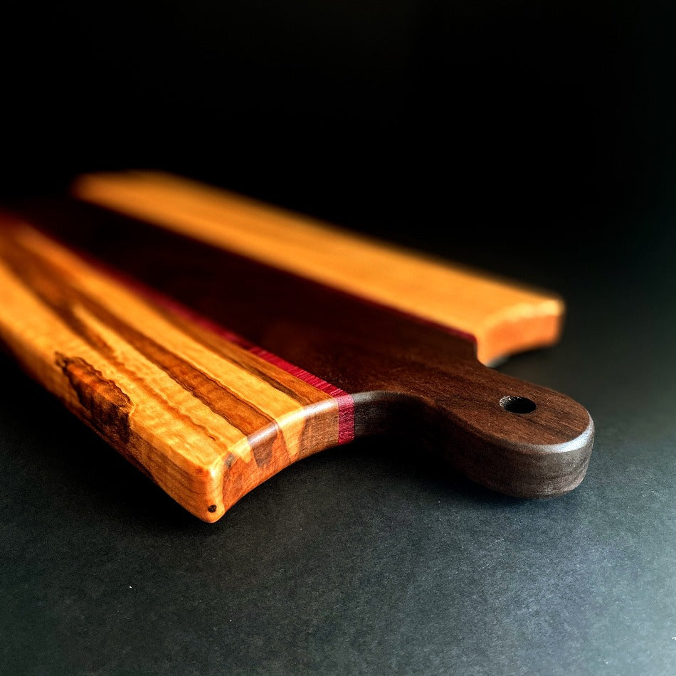 The Handcrafted Charcuterie Board or Bread Board is crafted from Walnut, Curly Tiger Heart and Purple Heart, measuring 18 x 8 x 1. This combination of woods offers remarkable depth. It is then seasoned with Milie's Tung Oil.