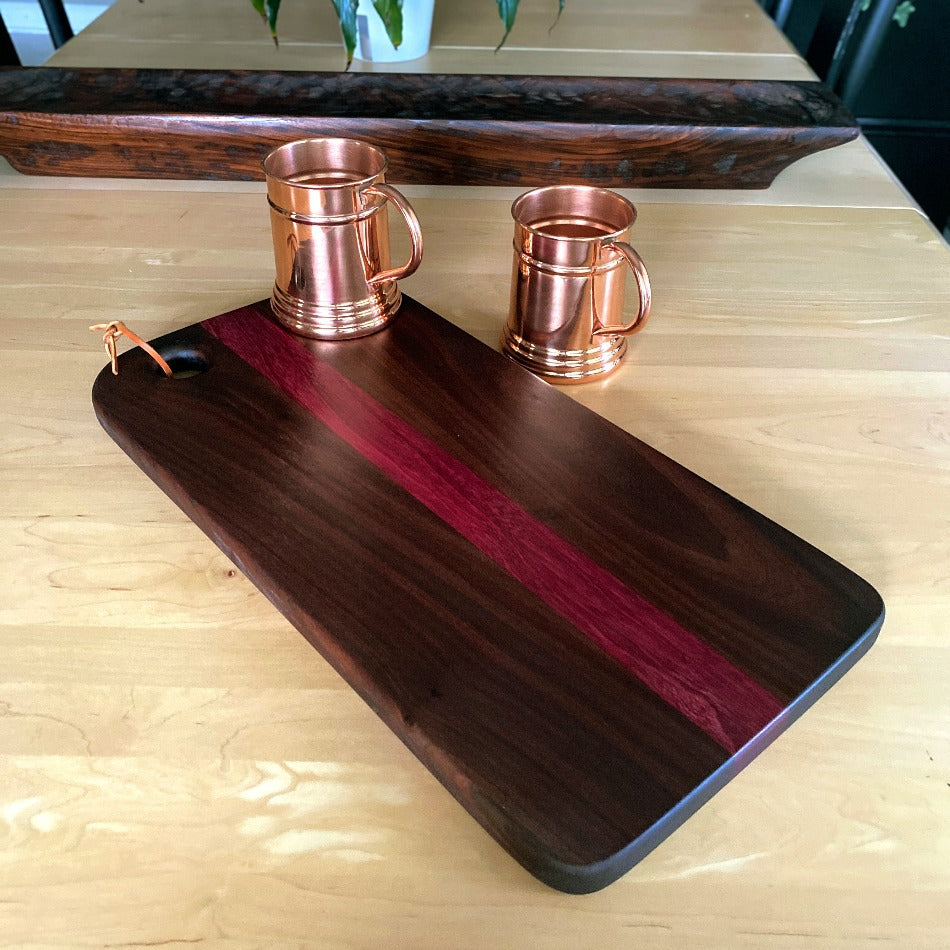 This handcrafted charcuterie board is the perfect way to impress guests. It's made with walnut and purple heart wood to create a stunning contrast of colors, which adds a simple, yet elegant touch to any presentation.