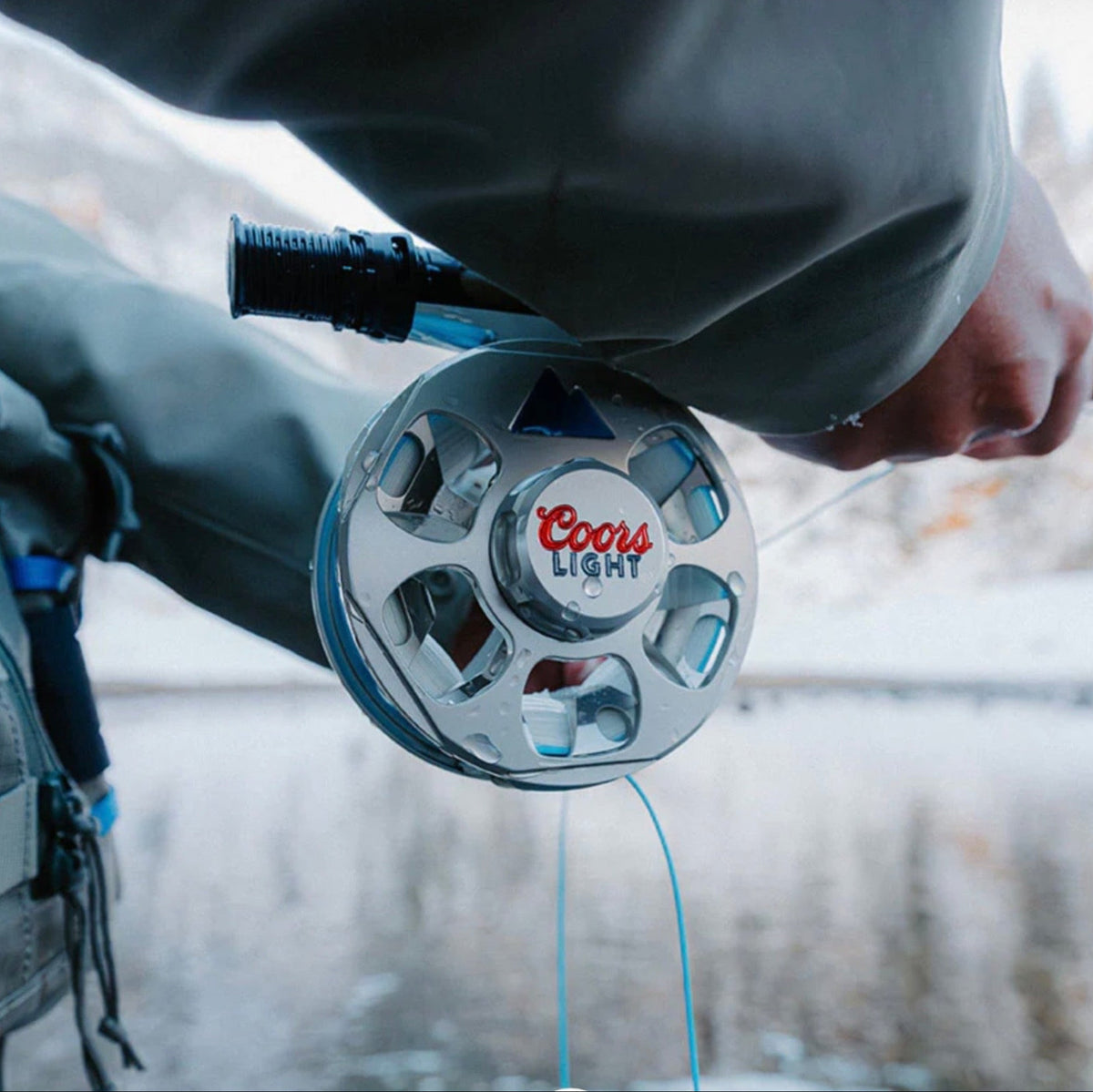 Fishing reel with Coors Light logo held by a person outdoors