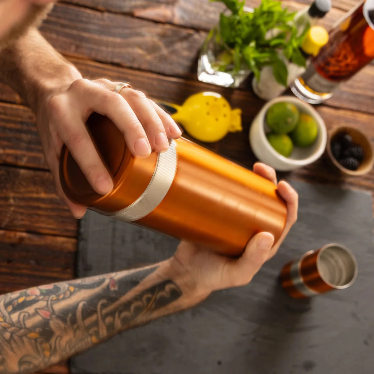 Person holding a copper-colored tumbler with tattoos on a wooden table.