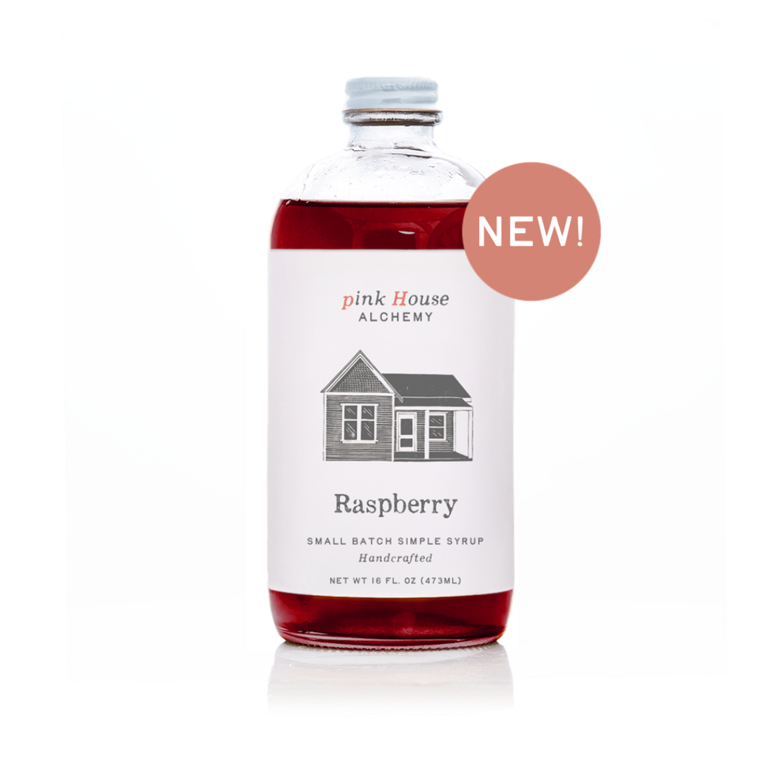 A bottle of Raspberry Simple Syrup from Pink House Alchemy, featuring a white label with a house illustration and a dusty pink 'NEW!' badge overlay on a white background.
