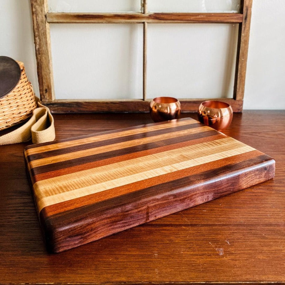 Edge Grain Serving Board - Fish On! Custom Rods Create a refined atmosphere at every gathering with this exquisite piece. Edge Grain Serving Board is 17 3/4" L, 12" W and 1 3/4" T. It's crafted with Leopard Wood, Padauk, Tiger Maple and Walnut.